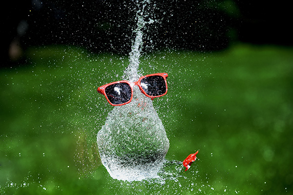 Ein mit Wasser gefüllter Luftballon platzt und hinterlässt den schwebenden Eindruck eines Wassergesichtes mit Sonnenbrille